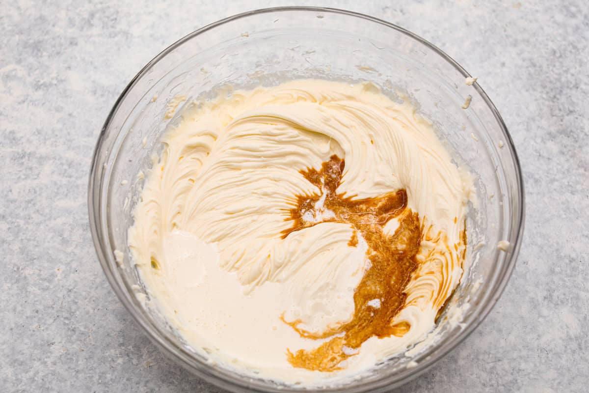 I am so excited about this recipe, it combines two of my all-time favorite desserts, cookie dough and cheesecake! With the rich Oreo crust, creamy cheesecake filling, and edible cookie dough bites, this no-bake cookie dough cheesecake will have your taste buds begging for more! Overhead shot of cheesecake filling mixture with vanilla extract poured on it.
