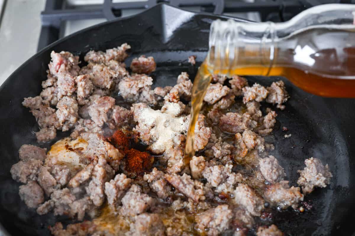 Beer and seasonings added to cooked sausage in a skillet. 