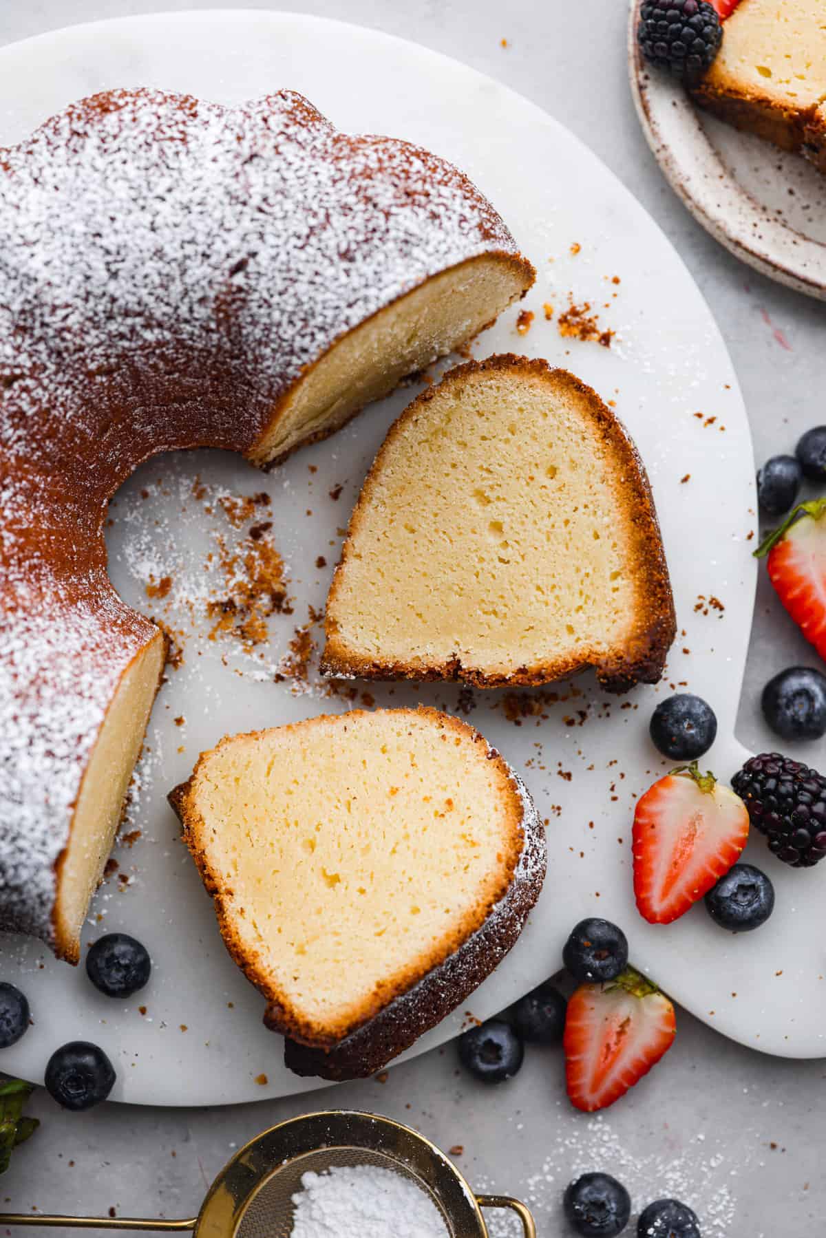 This Cream Cheese Pound Cake is a tender, moist, and flavorful dessert that's a new spin on traditional pound cake. Plus, it’s super simple to make! Top it off with whipped cream and fresh berries or enjoy plain! Top-down view of the cream cheese bundt cake with 2 slices cut out of it.