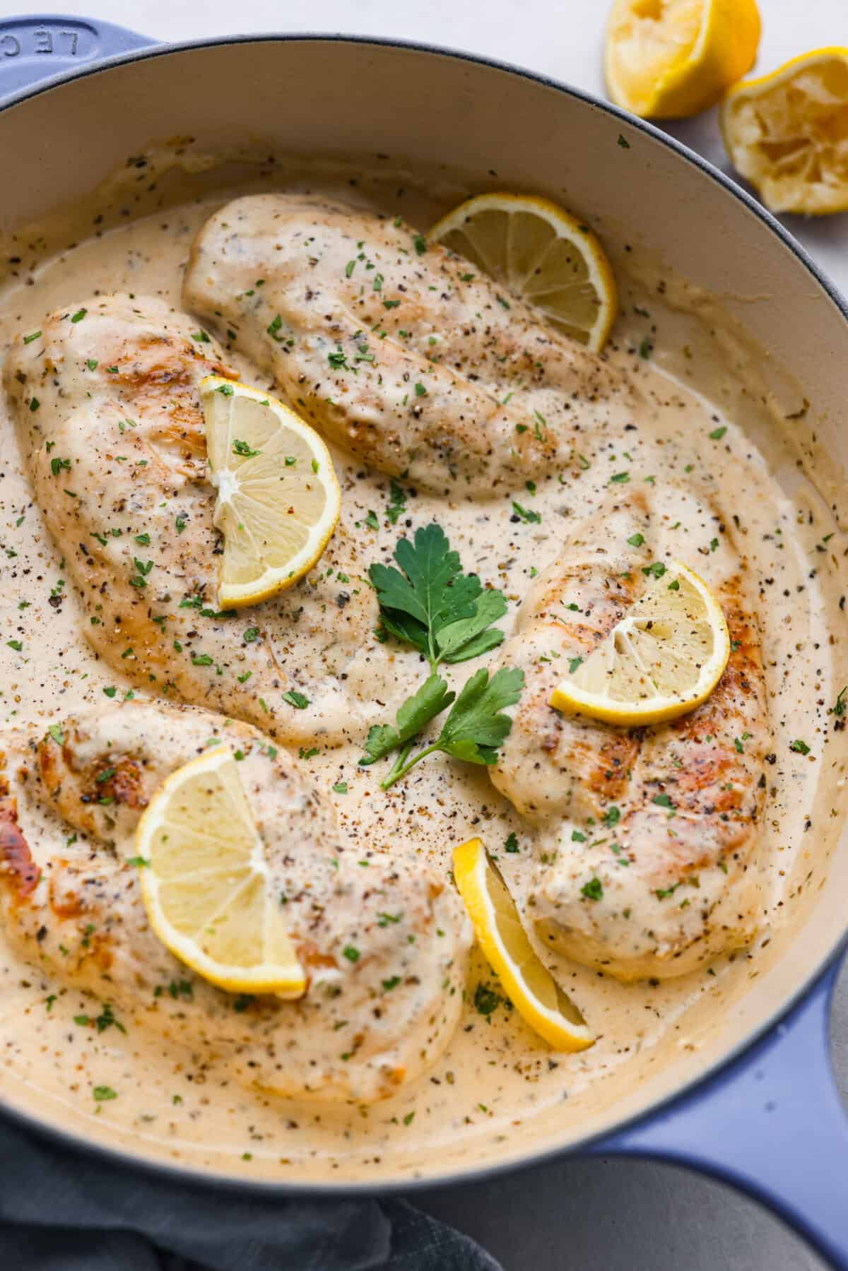 The finished creamy lemon parmesan chicken in a blue and white skillet, garnished with lemon slices and parsley.