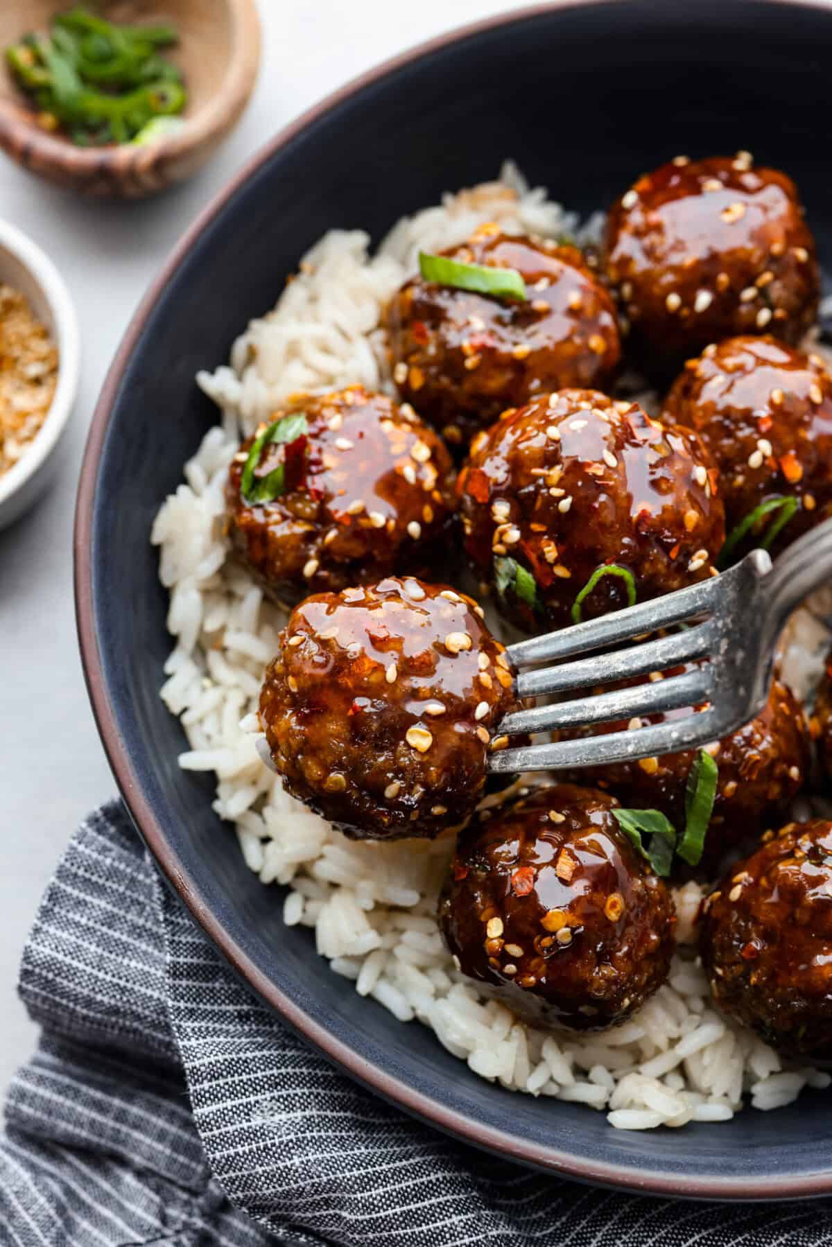Close up shot of plated rice and a fork skewering a meatball. 