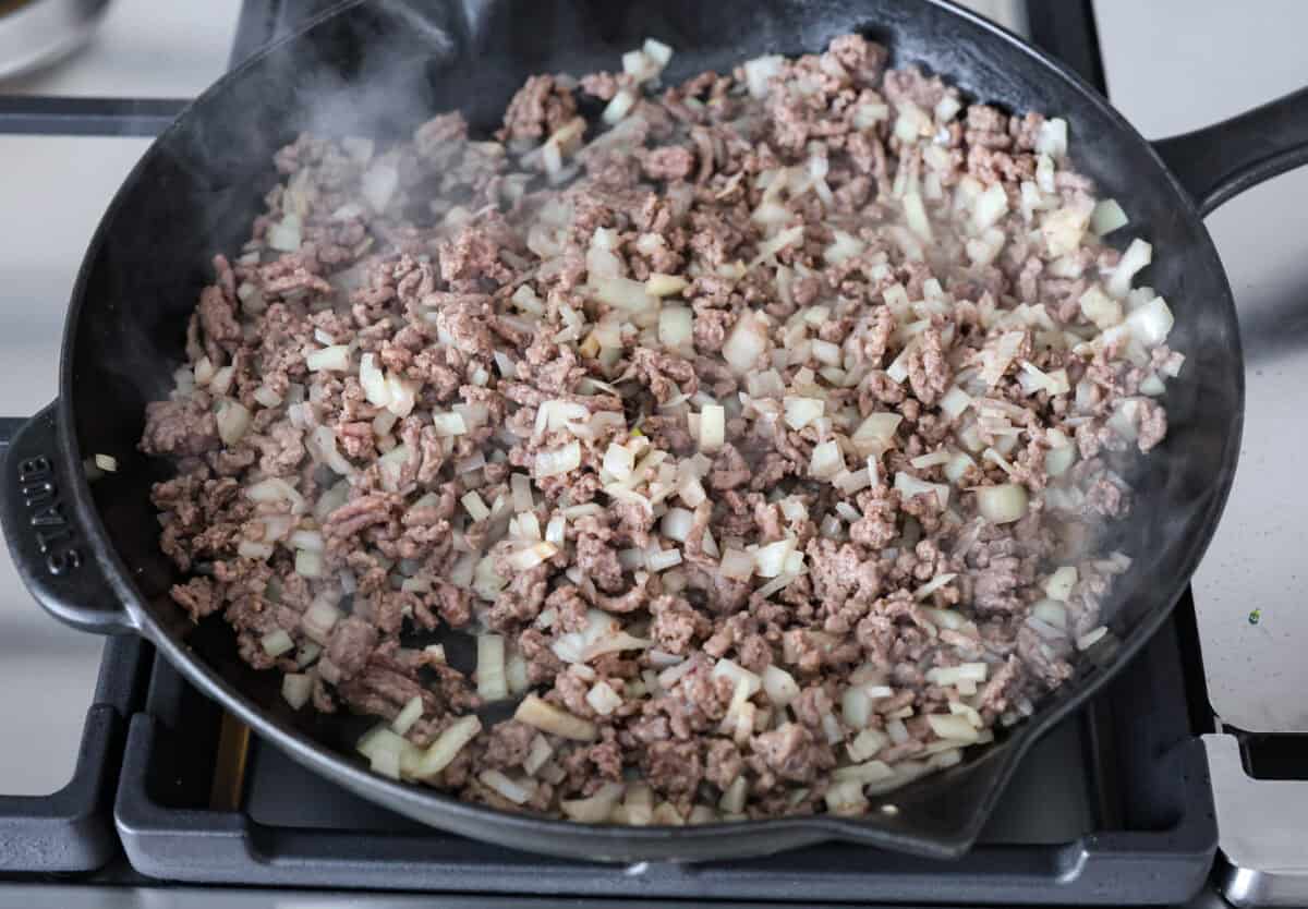 Overhead shot of ground beef with onions cooking in a skillet. 