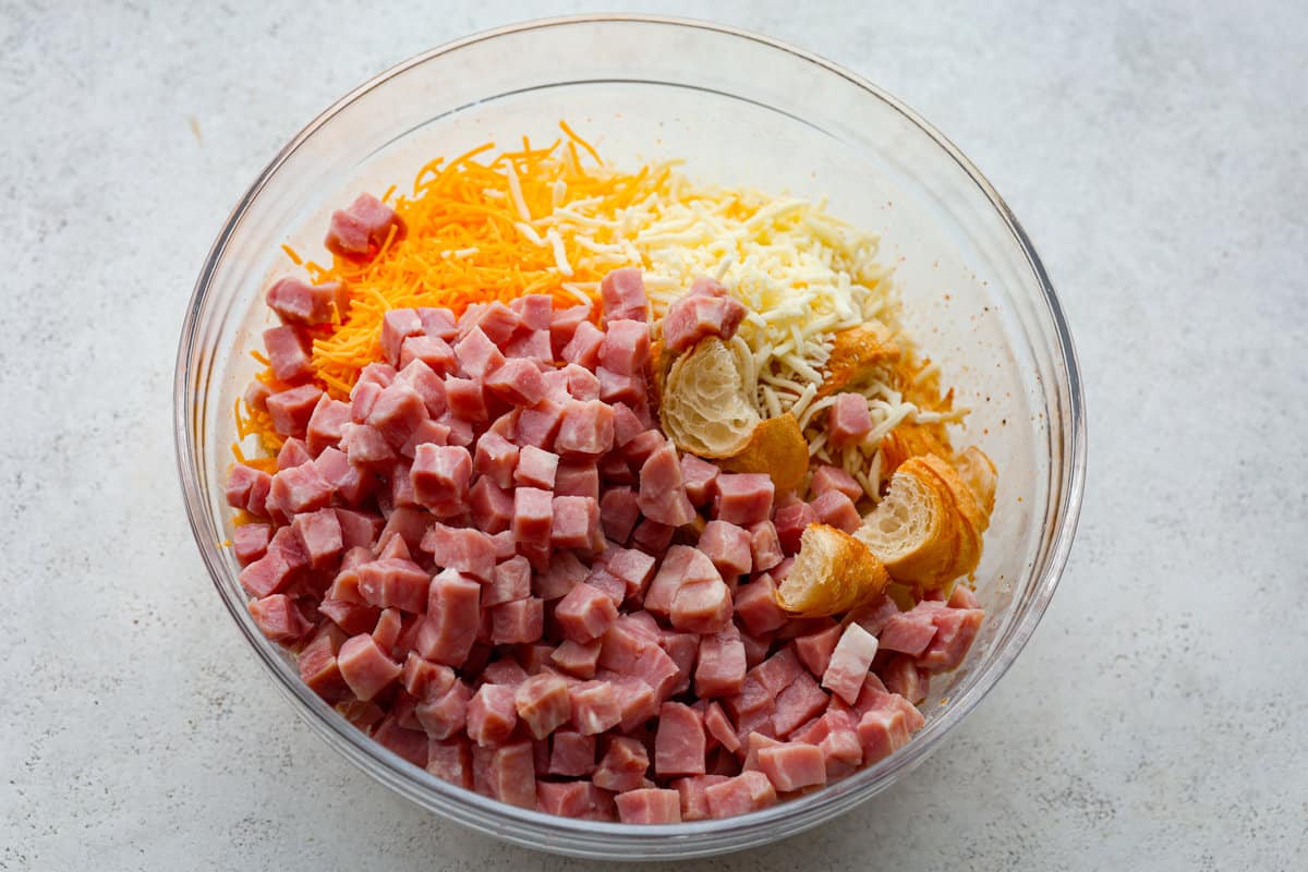 This Ham and Cheese Croissant Casserole is filled with comforting flavors of croissants, eggs, ham and plenty of melty cheese. It's quick and easy to throw together for a yummy dish that works for breakfast, lunch or dinner! Ham, cheese and croissants in a glass bowl.