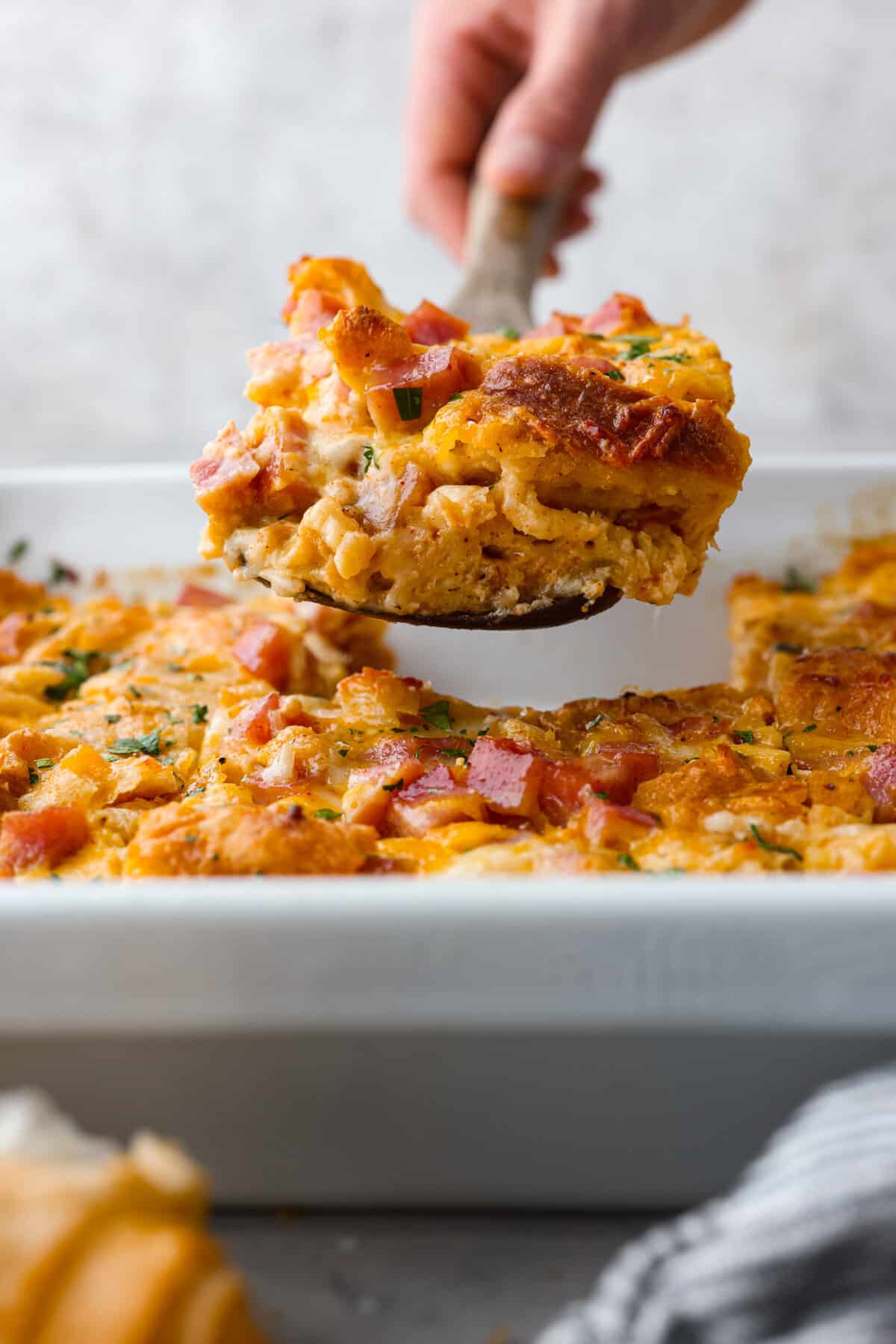 This Ham and Cheese Croissant Casserole is filled with comforting flavors of croissants, eggs, ham and plenty of melty cheese. It's quick and easy to throw together for a yummy dish that works for breakfast, lunch or dinner! The side view of a slice of casserole being served.