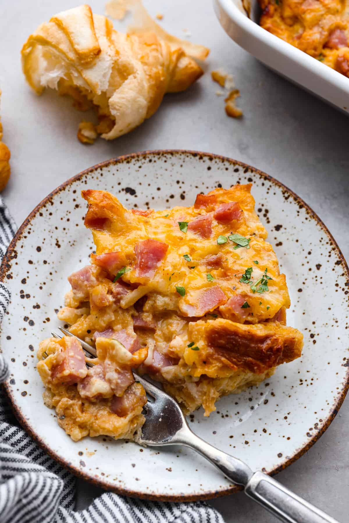 This Ham and Cheese Croissant Casserole is filled with comforting flavors of croissants, eggs, ham and plenty of melty cheese. It's quick and easy to throw together for a yummy dish that works for breakfast, lunch or dinner! The top view of ham and cheese croissant casserole on a plate.