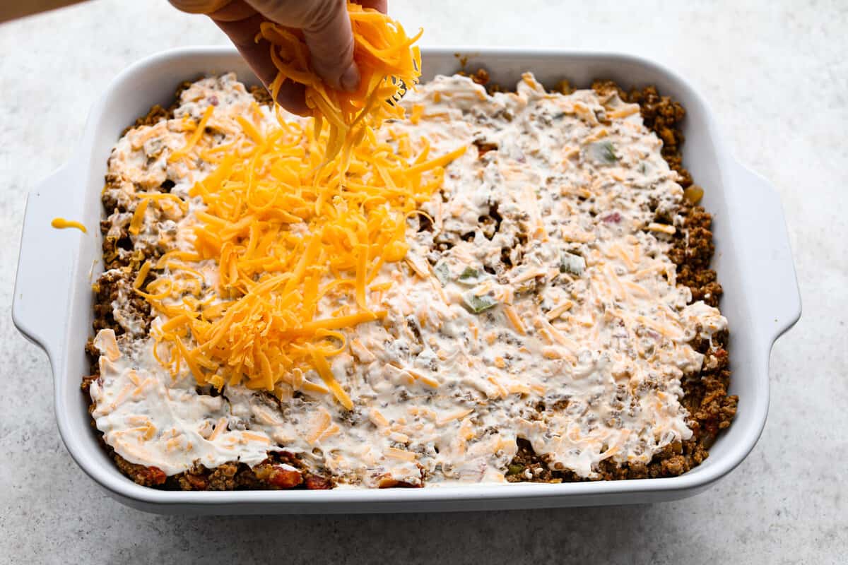 This delicious John Wayne Casserole is Mexican comfort food at its finest! Layers of seasoned ground beef, creamy cheddar cheese mixture, and more shredded cheese are baked on top of a biscuit crust for a crowd-pleasing family dinner! Cheese and mayonnaise mixture added to pan of John Wayne Casserole.