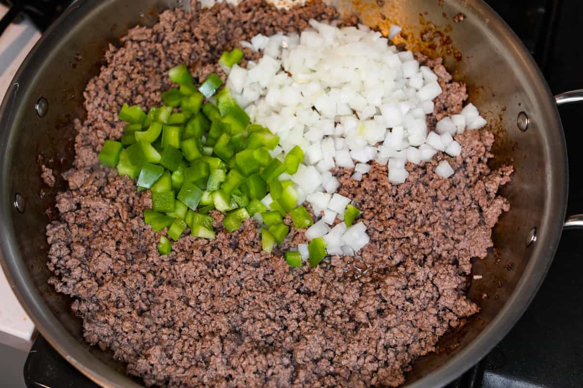 This delicious John Wayne Casserole is Mexican comfort food at its finest! Layers of seasoned ground beef, creamy cheddar cheese mixture, and more shredded cheese are baked on top of a biscuit crust for a crowd-pleasing family dinner! Cooked ground beef on the stove with onions and peppers being added.