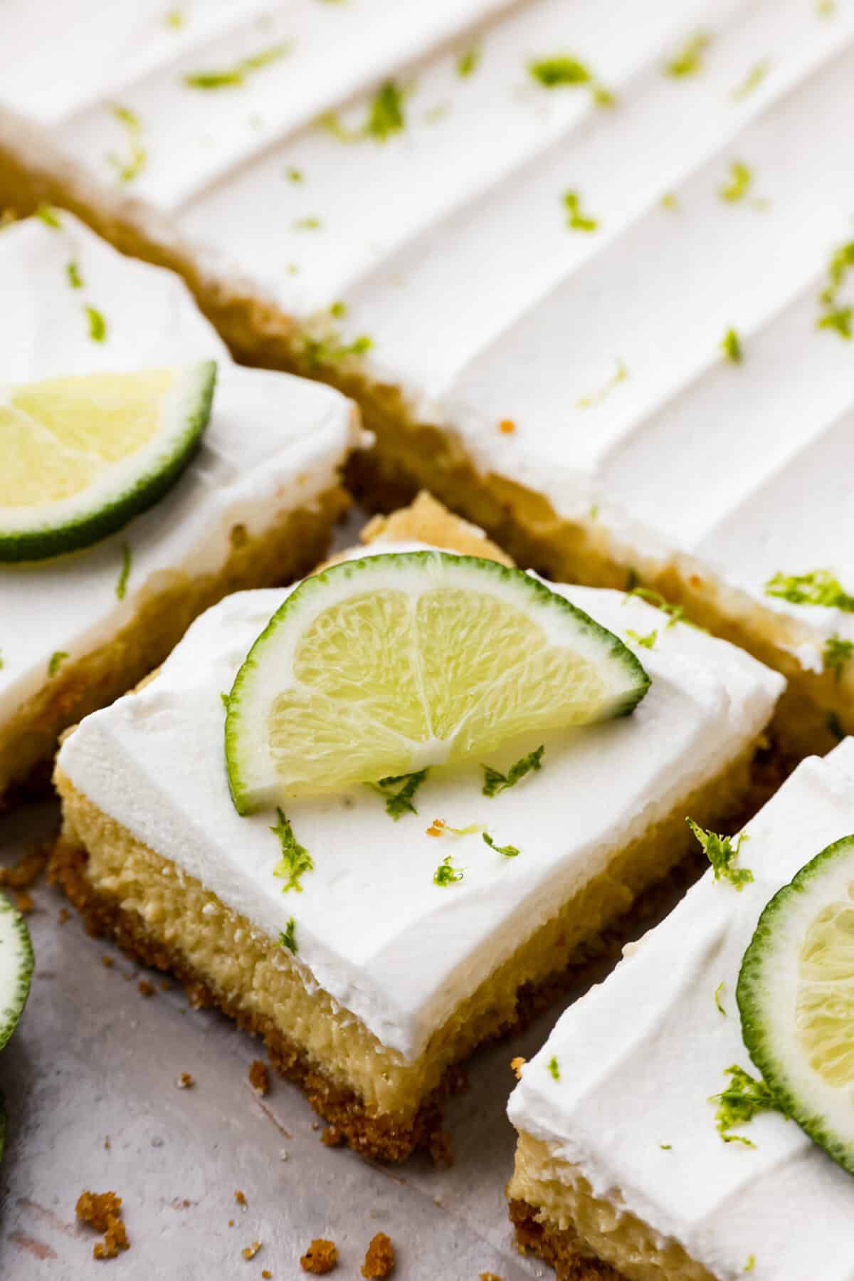 Close view of key lime pie bars cut and garnished with lime slices and zest.