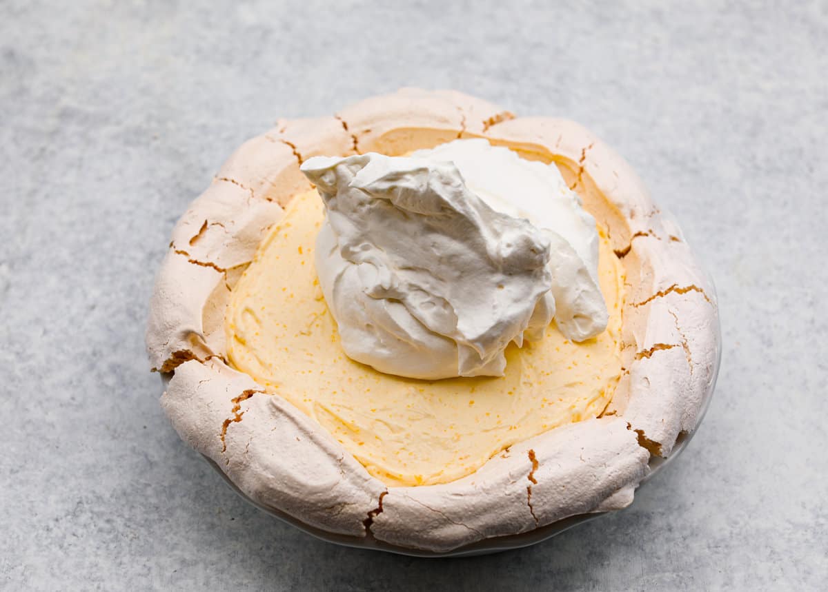 Lemon angel pie is a delightful dessert straight from heaven! It has a creamy lemon filling inside a sweet, airy meringue crust, then topped with fresh whipped cream. Every bite is pure bliss! Sixth process photo of the remaining whipped cream being spread on top of the lemon angel pie.