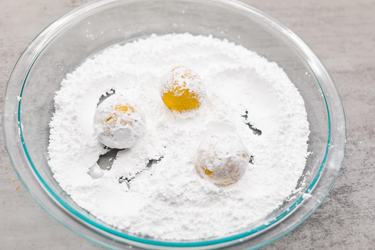 Lemon crinkle cookies are thick, soft pillows of lemon deliciousness! They have a refreshing flavor with an irresistible chewy texture. The perfect balance of sweet and tart make these a welcome treat for any occasion! Rolling the unbaked lemon crinkle cookies in powdered sugar.