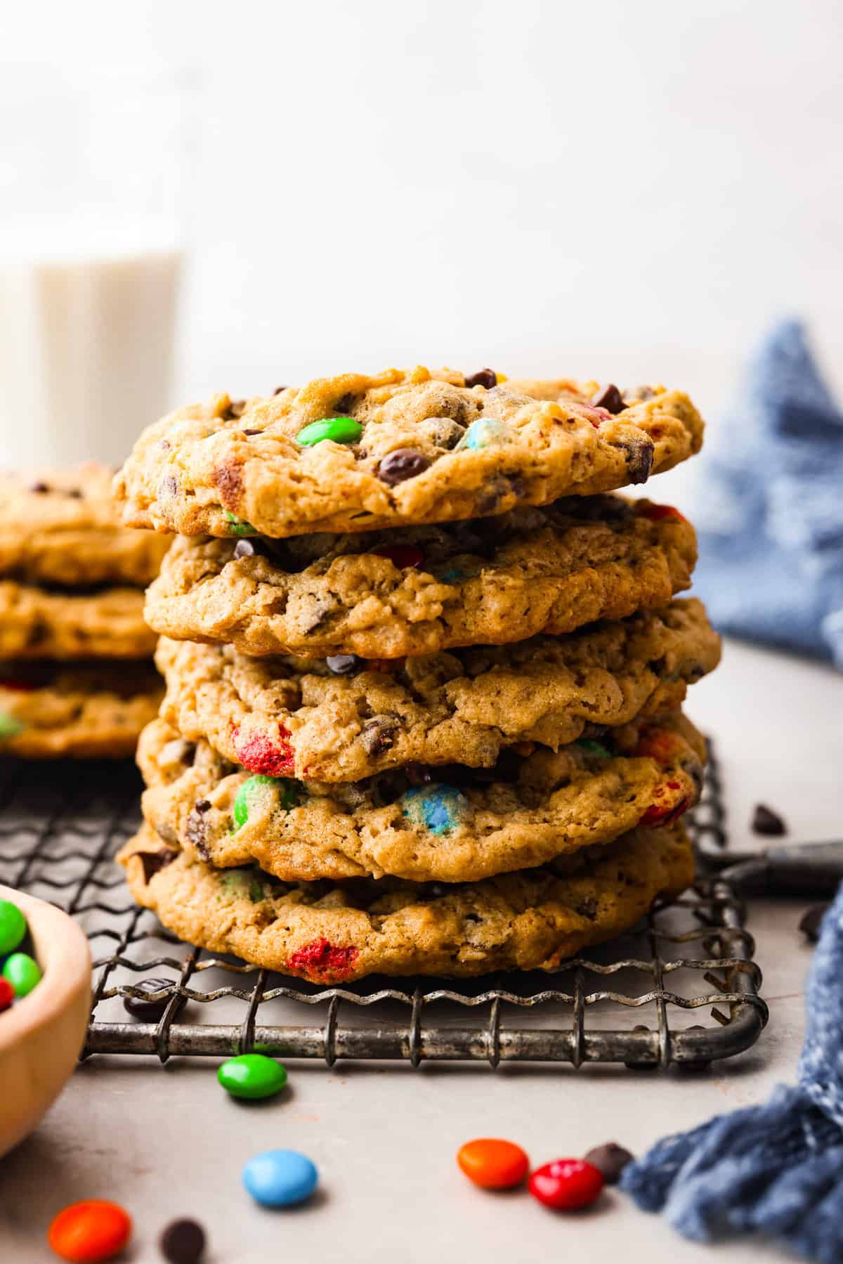 Monster cookies are slightly crisp on the outside, and soft and chewy in the center. They are loaded with peanut butter, oats, M&M candies, AND chocolate chips! Big monster cookies win every time! Close photo of monster cookies stacked on a cooling rack.
