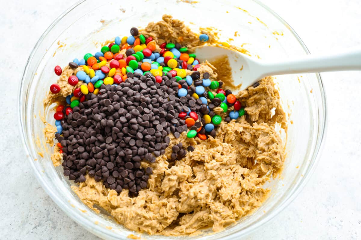 Process photo of cookie dough mixed with M&M's and chocolate chips added to the bowl.