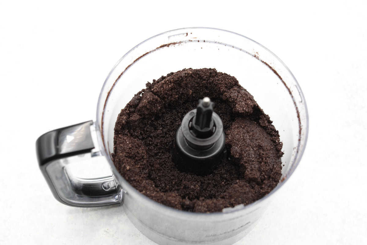 I am so excited about this recipe, it combines two of my all-time favorite desserts, cookie dough and cheesecake! With the rich Oreo crust, creamy cheesecake filling, and edible cookie dough bites, this no-bake cookie dough cheesecake will have your taste buds begging for more! Overhead shot of food processor with crushed Oreos and butter mixed.
