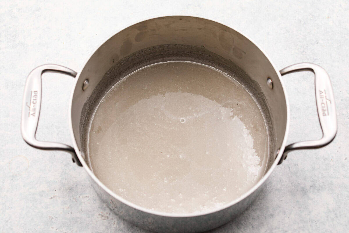 Overhead shot of a silver pot with water, gelatin and sugar in it sitting on the counter. 
