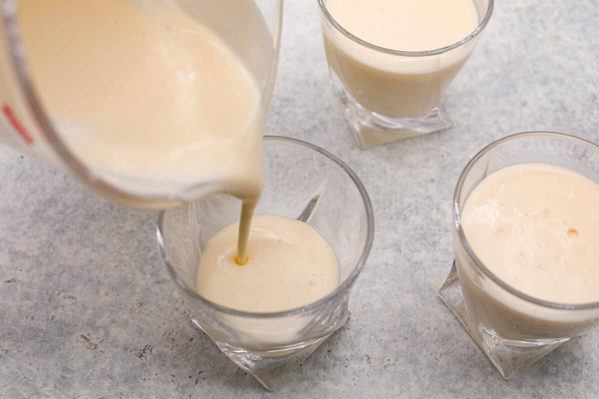 Overhead shot of individual cups of cream mixture, with one having cream mixture being poured into it. 