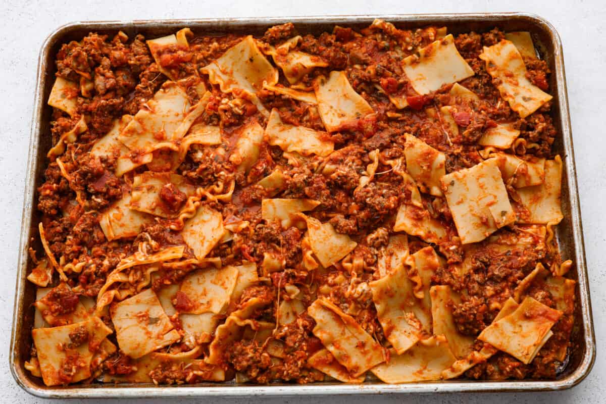 Lasagna noodles and meat being spread on a sheet pan. 