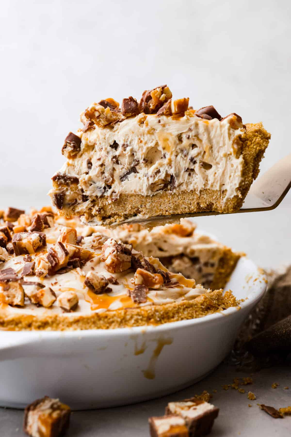 A slice of no bake snickers bar pie being removed from the pie pan. 