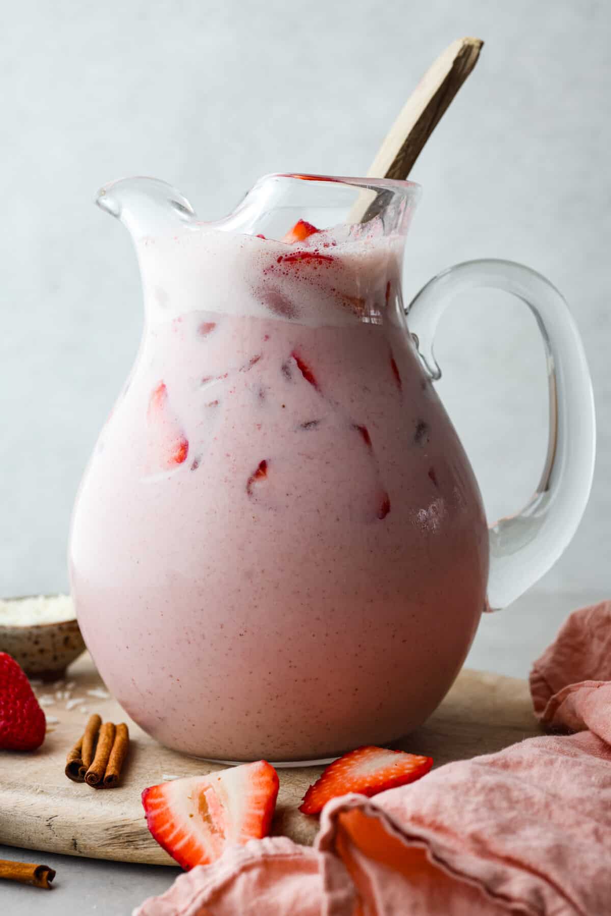 Close view of strawberry horchata in a glass pitcher with a large gold spoon for stirring. 