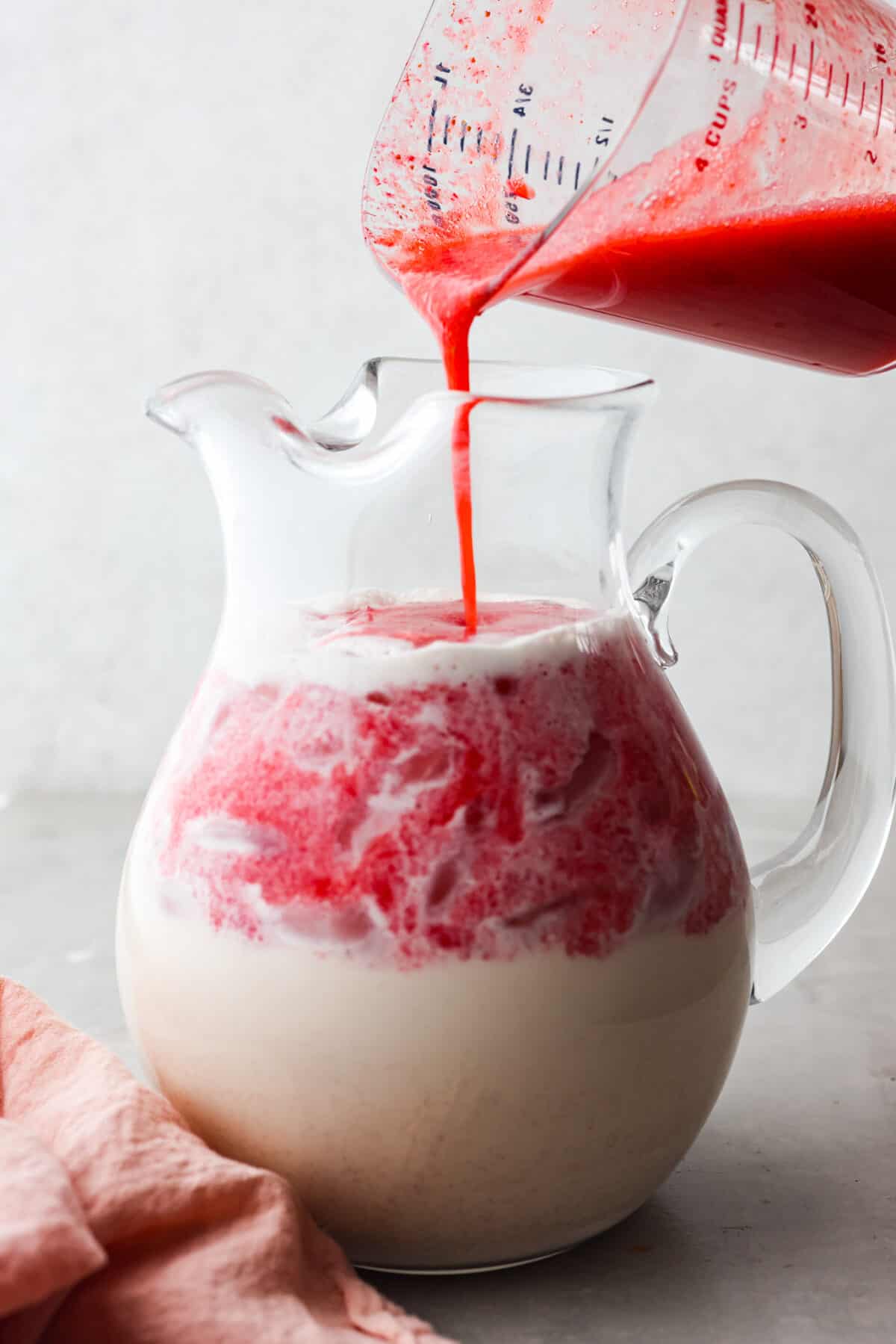 Close view of a large glass pitcher full of horchata with the strawberry puree pouring in.