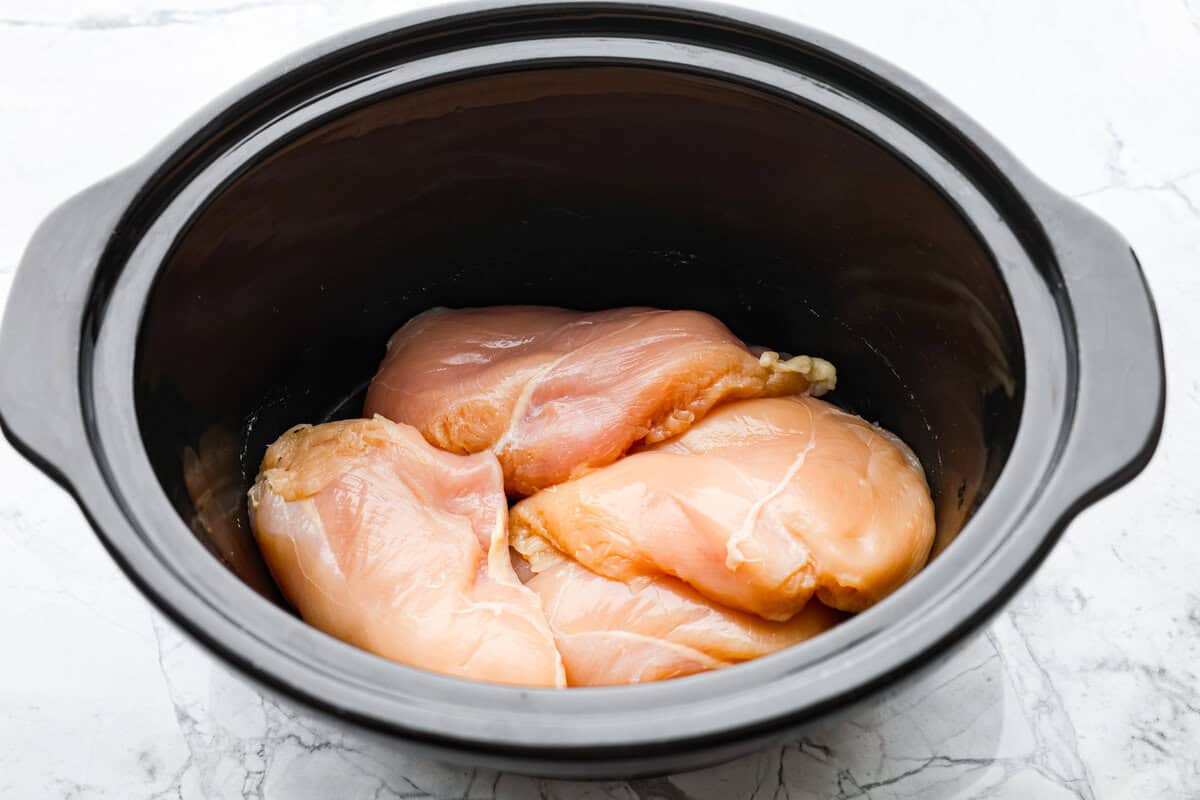 This zesty BBQ chicken is an easy crockpot recipe that only takes 5 ingredients to make! The slow-cooked tender pulled chicken is dripping in a tasty BBQ sauce. Perfect for busy weeknights or to feed a crowd! First photo of chicken placed in the bottom of the crockpot.