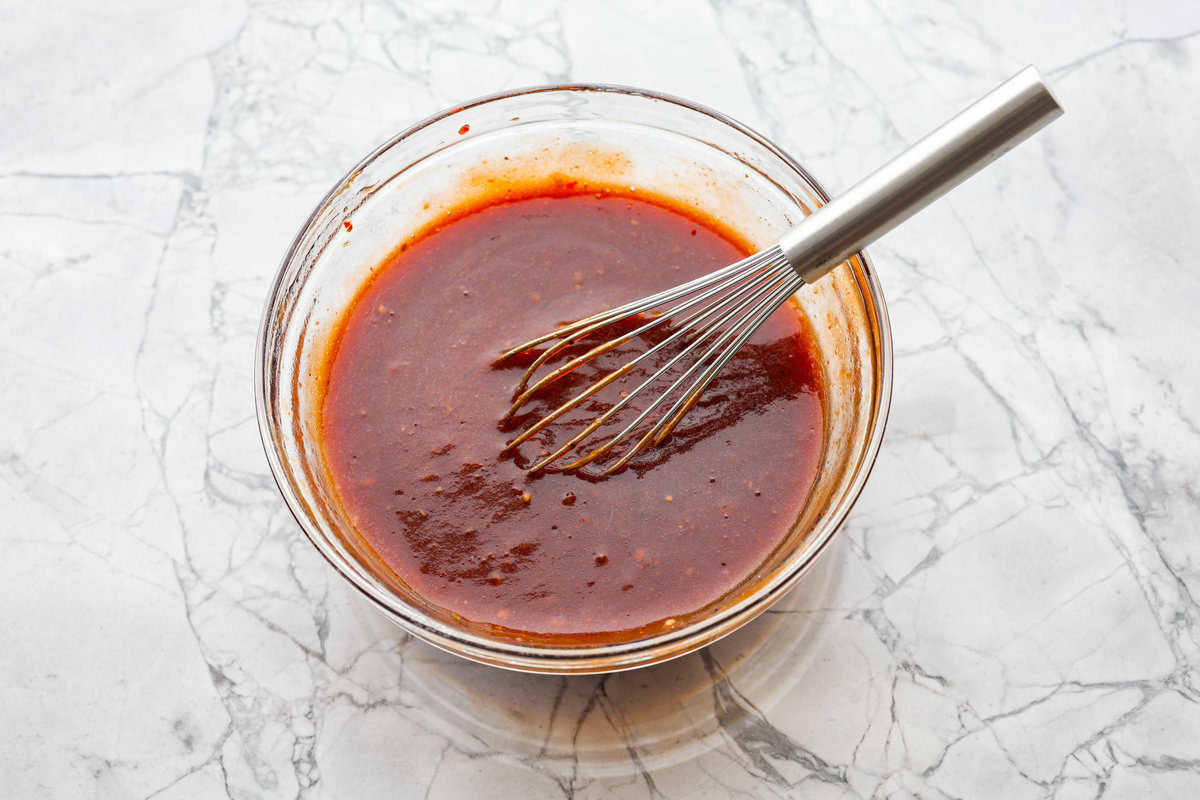 This zesty BBQ chicken is an easy crockpot recipe that only takes 5 ingredients to make! The slow-cooked tender pulled chicken is dripping in a tasty BBQ sauce. Perfect for busy weeknights or to feed a crowd! Third photo of the bbq sauce whisked in a bowl.