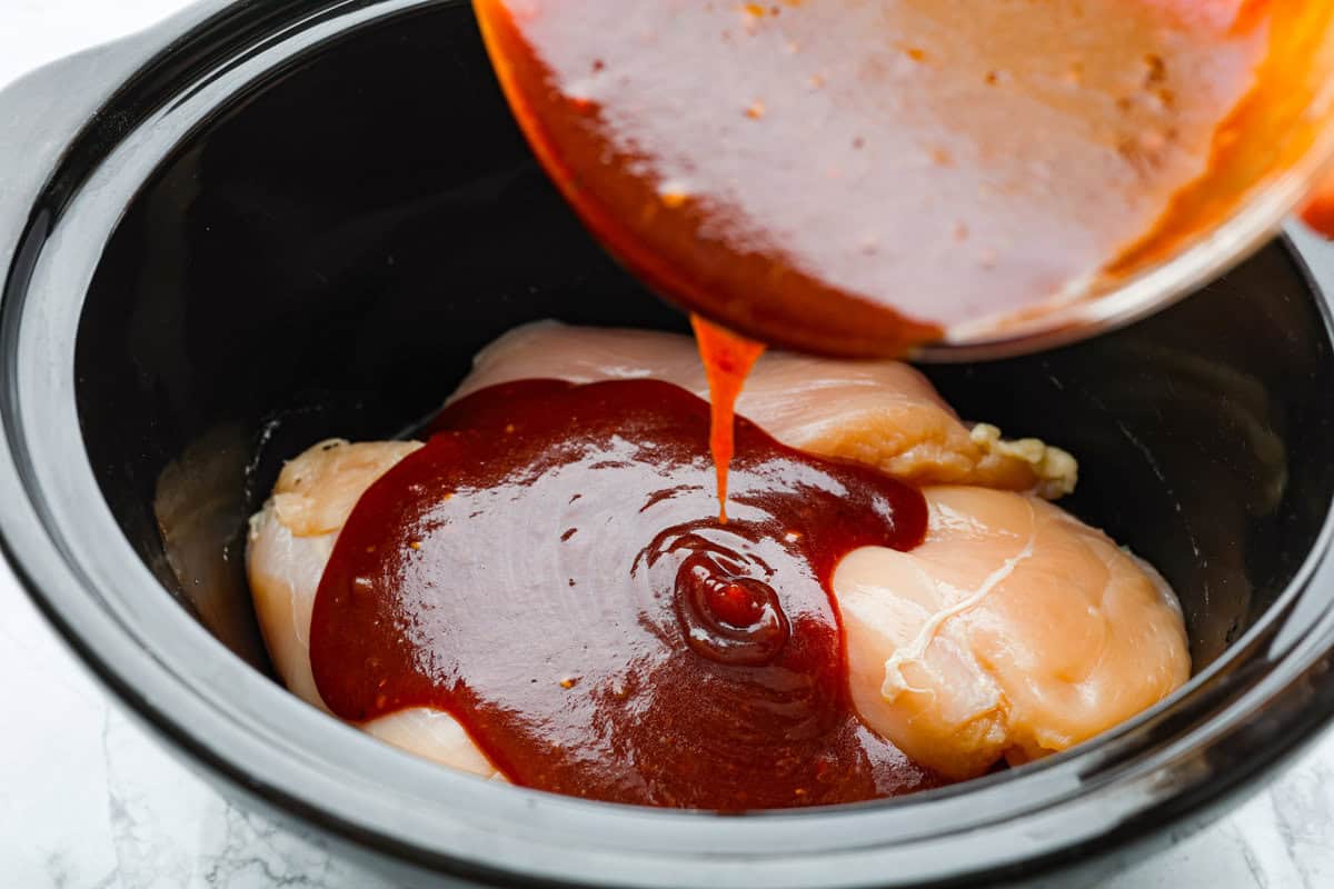 This zesty BBQ chicken is an easy crockpot recipe that only takes 5 ingredients to make! The slow-cooked tender pulled chicken is dripping in a tasty BBQ sauce. Perfect for busy weeknights or to feed a crowd! Fourth photo of the bbq sauce pouring over the chicken.