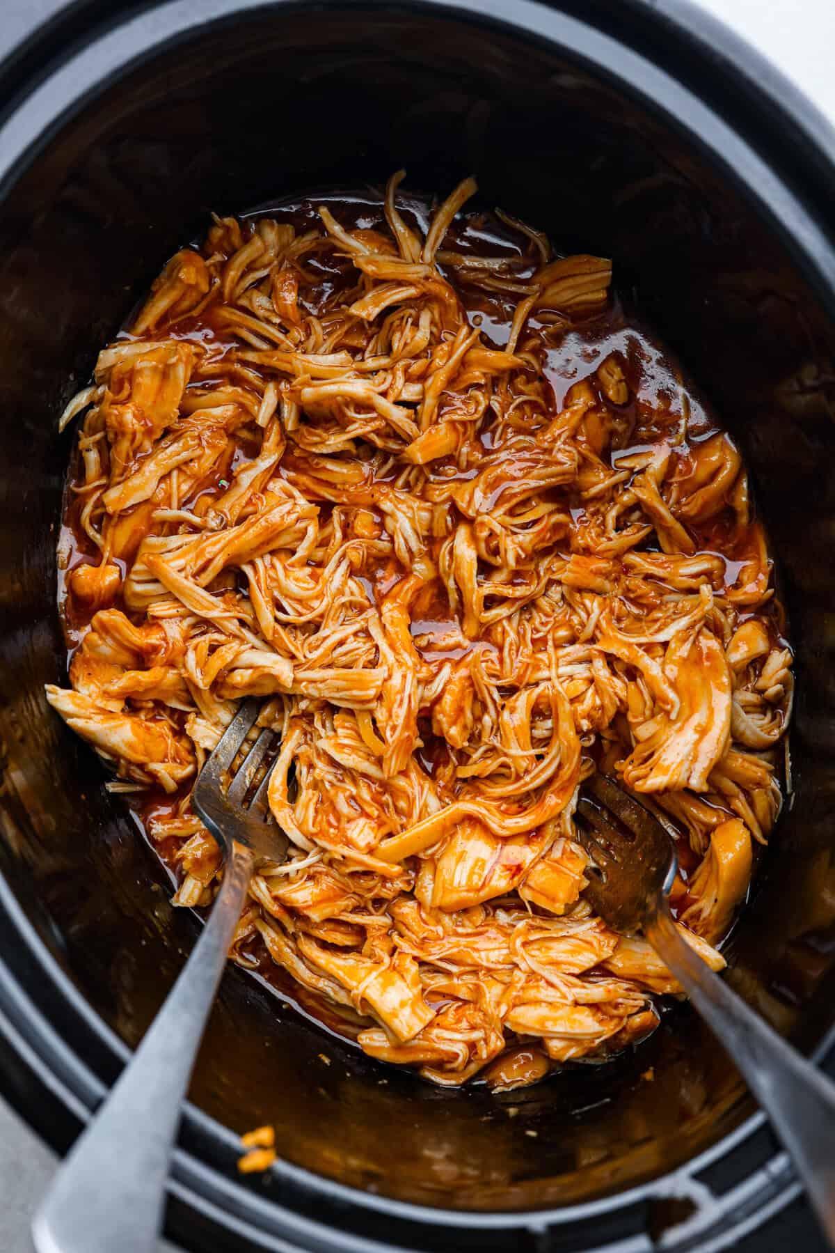 This zesty BBQ chicken is an easy crockpot recipe that only takes 5 ingredients to make! The slow-cooked tender pulled chicken is dripping in a tasty BBQ sauce. Perfect for busy weeknights or to feed a crowd! Top view of zesty bbq chicken shredded in the crockpot.