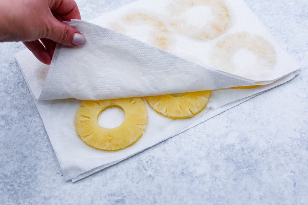 Third photo of the pineapple rings being pressed into a paper towel.