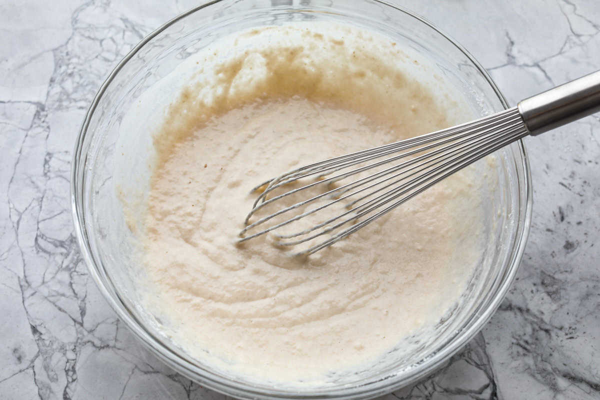 Whip up a batch of these delightful zeppole, perfect for a sweet treat anytime! With a light, fluffy texture and a generous coating of powdered or cinnamon sugar, these Italian donuts are sure to please. Overhead shot of wet and dry ingredients for zeppoles all mixed together in a bowl with a whisk.