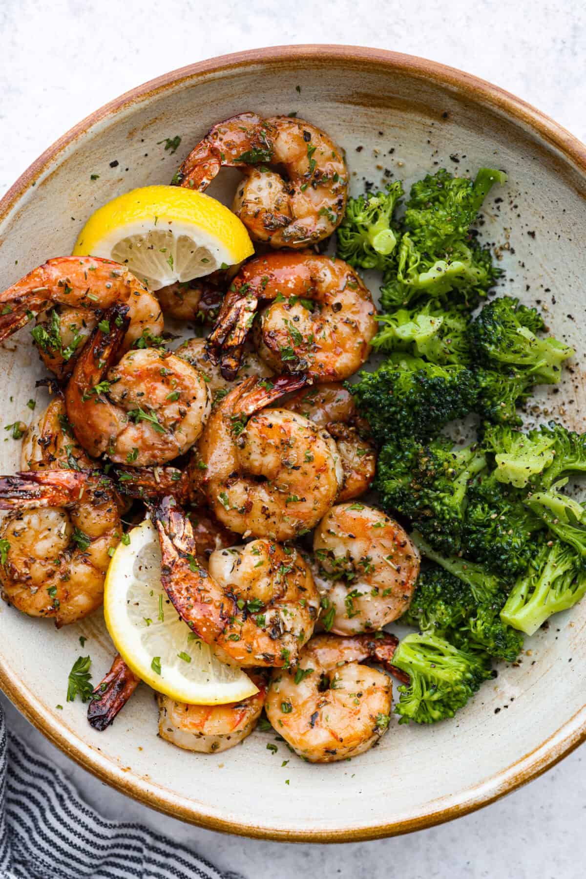 Top view of air fryer shrimp in a bowl with broccoli and garnished with lemon.
