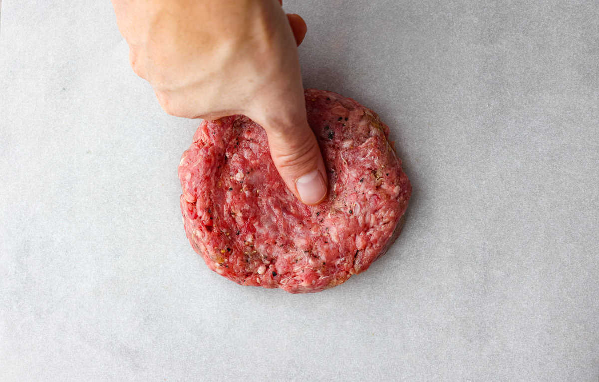 Get ready for the ultimate burger experience topped with my irresistible Secret Sauce. The flavor packed into this burger is a delicious twist on a classic favorite. Someone indenting the ground beef with their thumb.