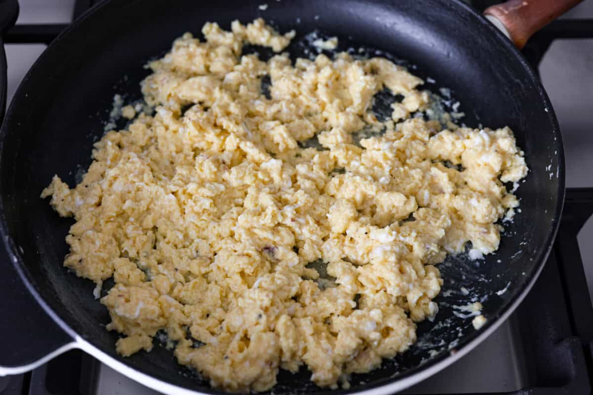 Overhead shot of eggs being cooked scrambled in a pan on a stovetop. 