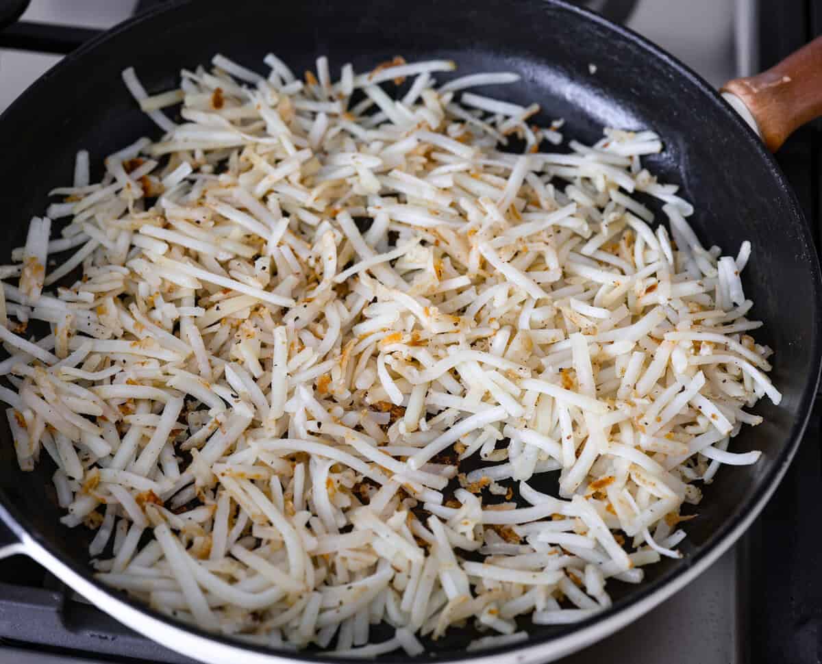 Breakfast Egg Rolls are a fun and delicious way to change up breakfast! The inside is filled with savory sausage, creamy eggs, hash browns, and plenty of cheese. Fry them up for a gooey, tender, savory center and a delicately crunchy exterior. This is a fun and unique breakfast that everyone will love! Overhead shot of hash browns being cooked in pan,