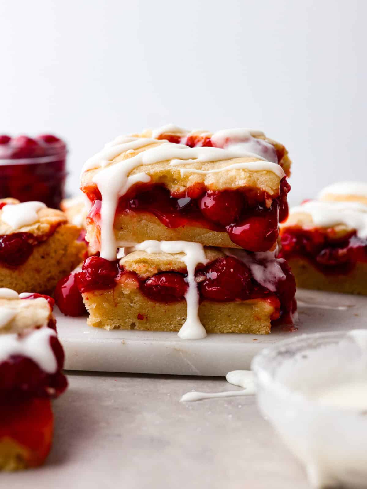 A stack of cherry pie bars with the glaze drizzling off. 