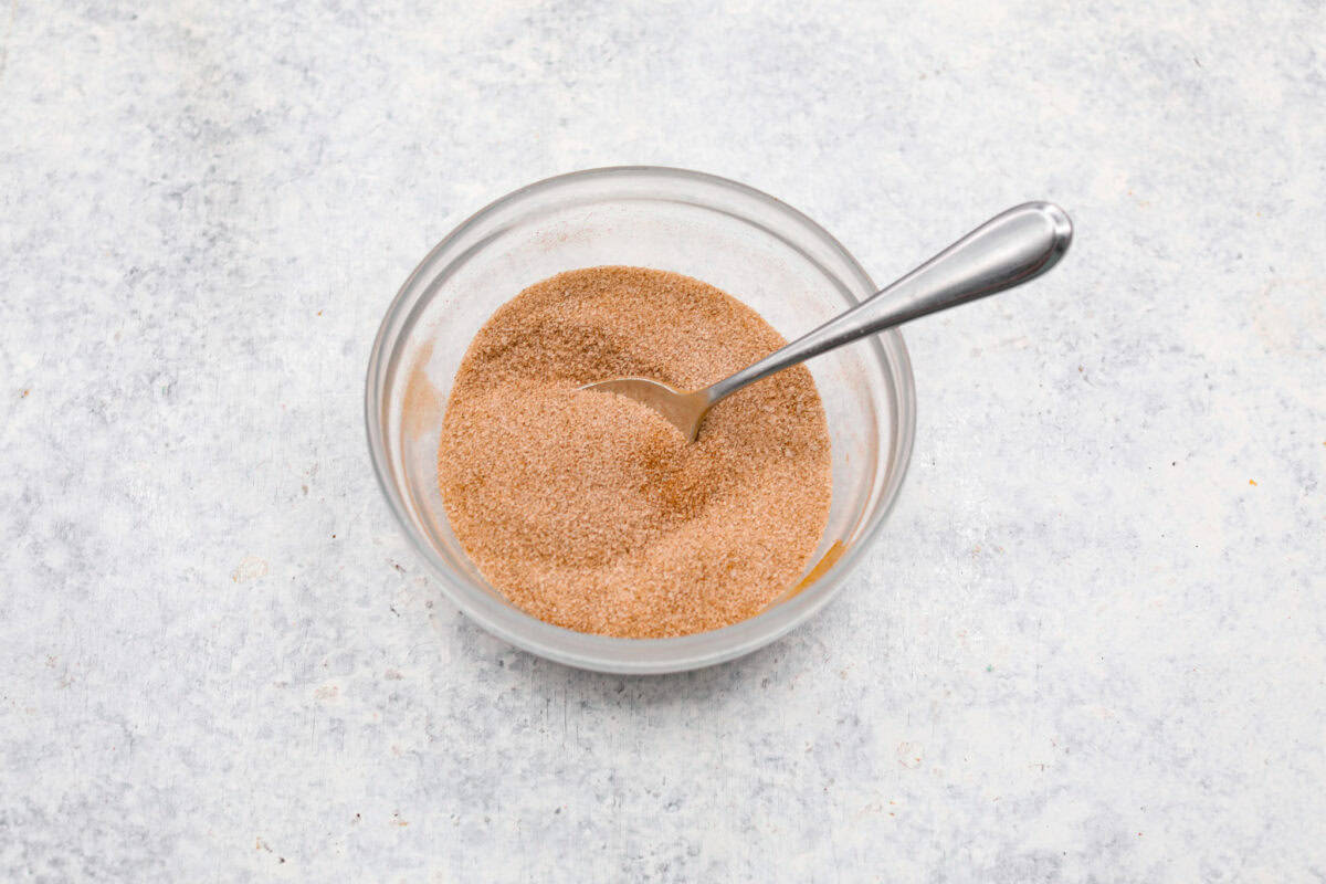 Small glass bowl with cinnamon and sugar mixed together with a spoon. 