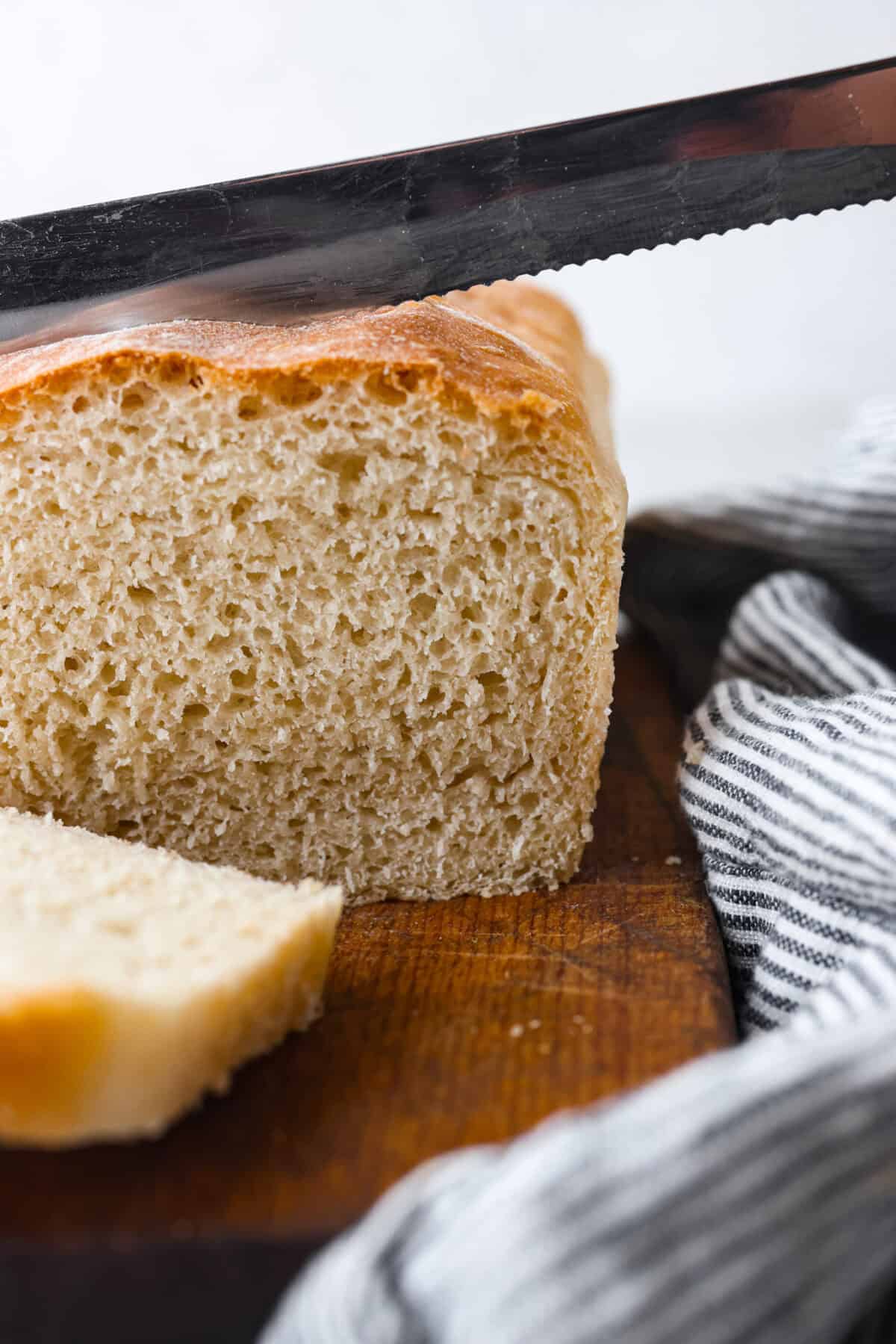 Close view of a serrated knife slicing a loaf of bread.