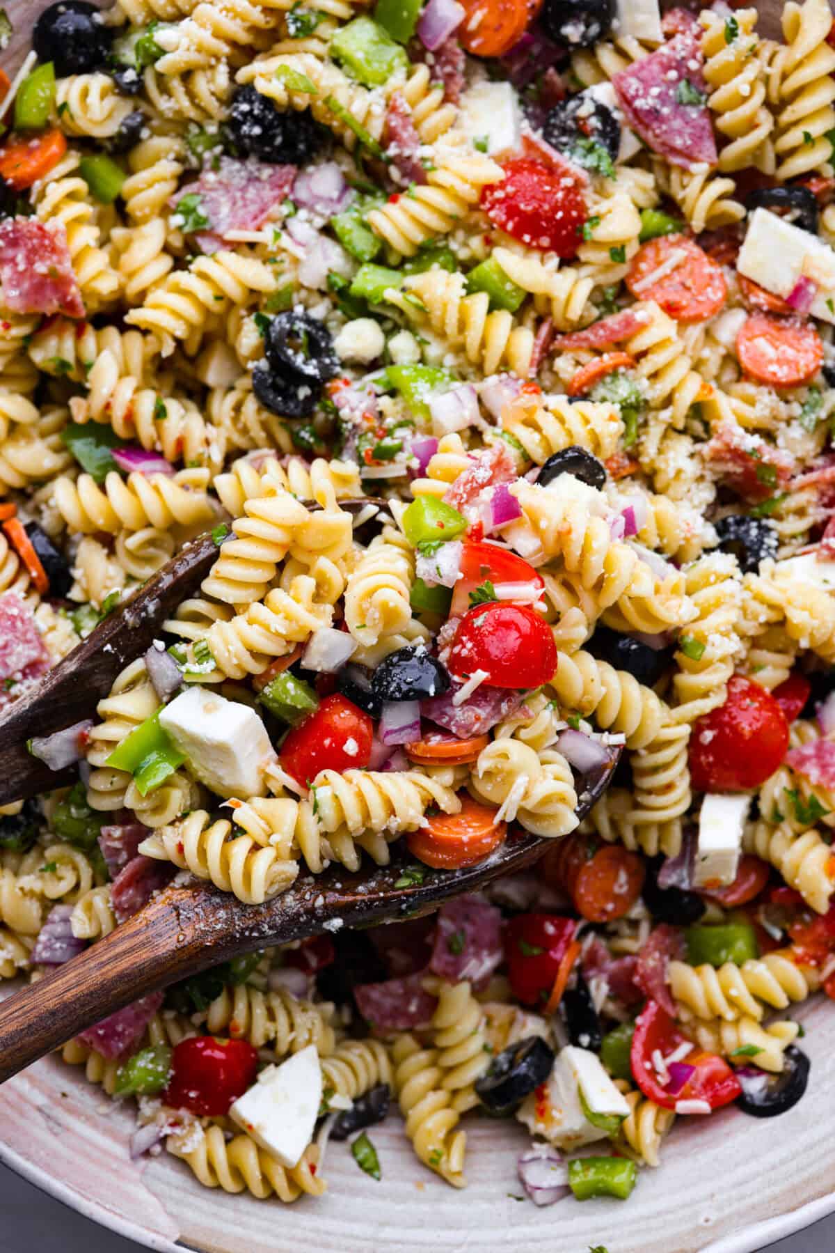 Close up shot of pasta salad with  rotini noodles, tomatoes, bits of red onion, olives, salami, green pepper and cheese. 