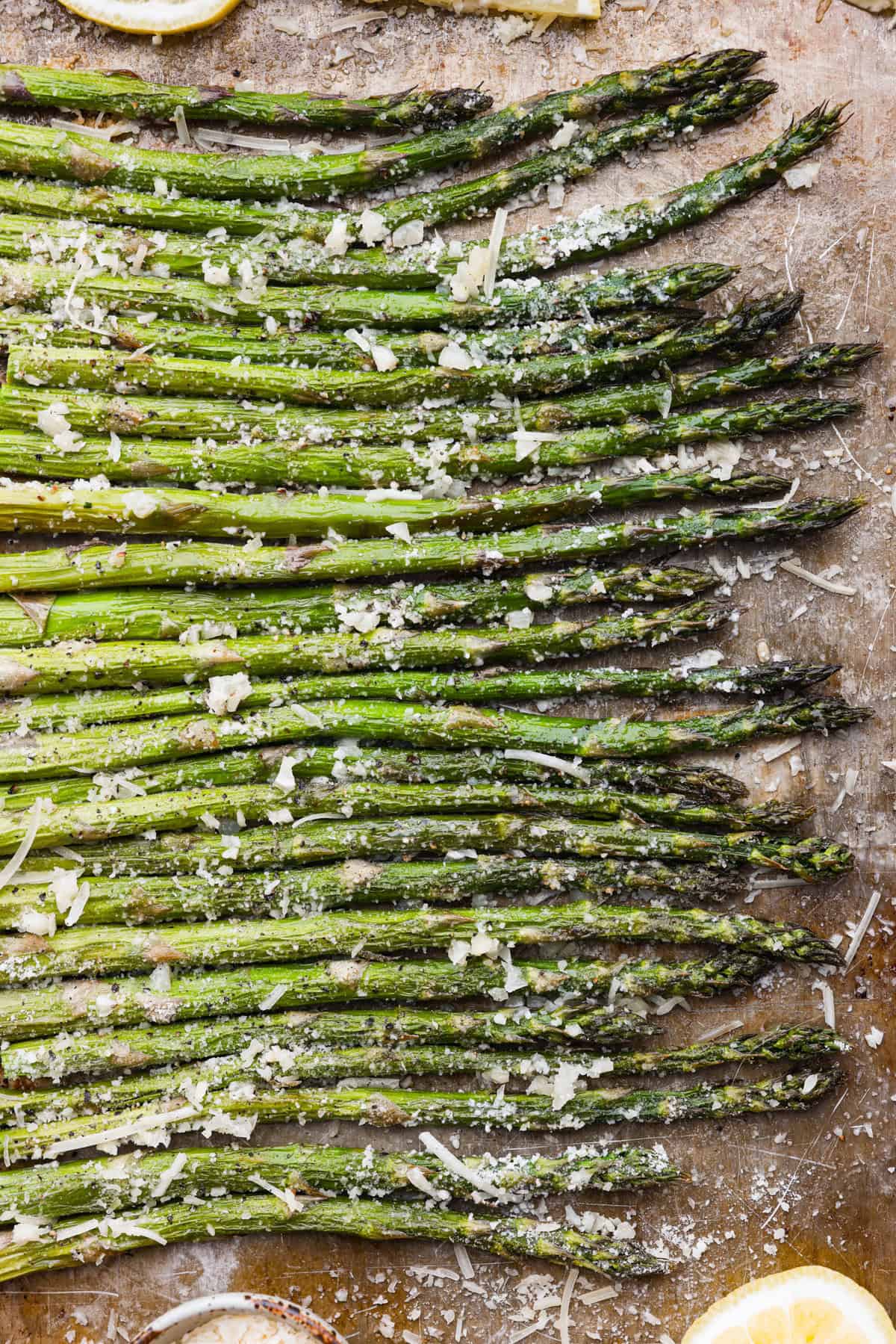 You'll love the combination of flavors in this roasted lemon parmesan garlic asparagus! It's a quick and easy side dish bursting with parmesan, garlic, and a hint of lemon to brighten it all. This is a side that you will make again and again! Top close view of roasted lemon parmesan garlic asparagus on a sheet pan.