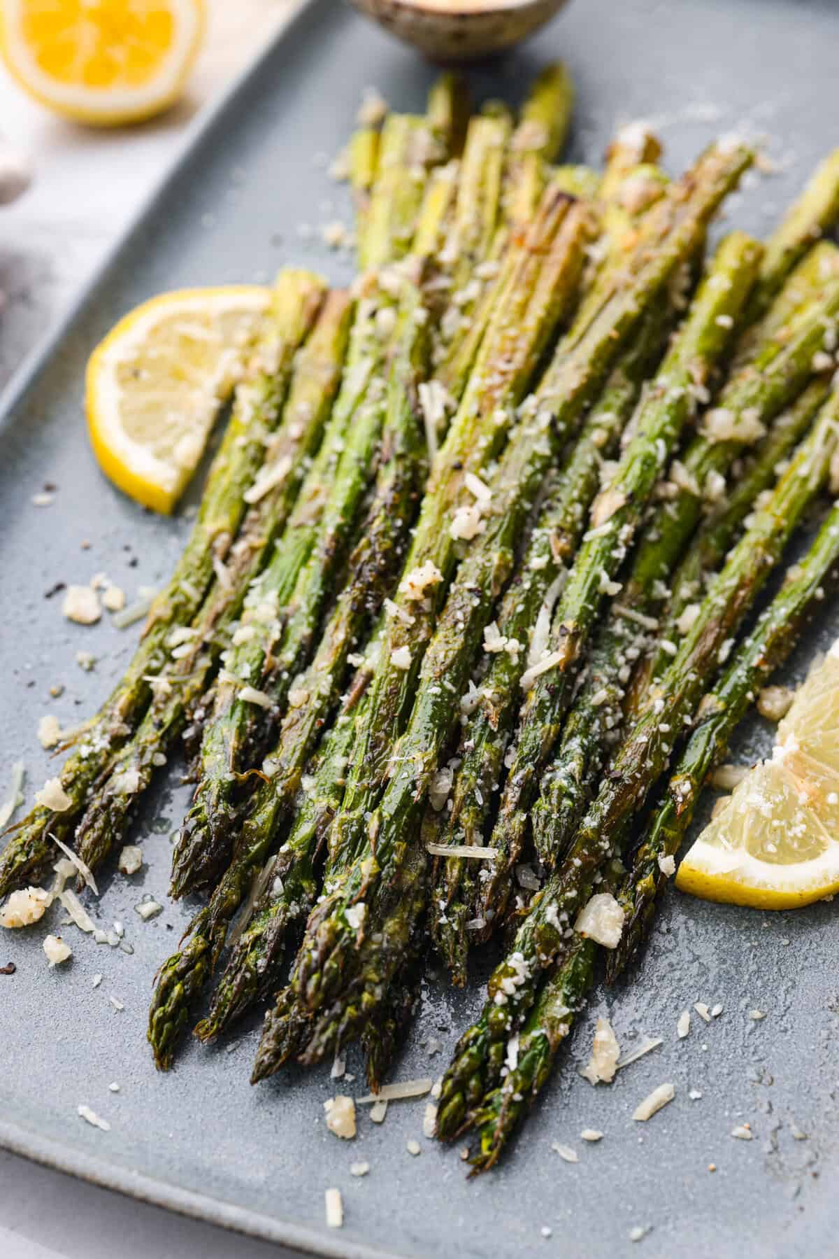 You'll love the combination of flavors in this roasted lemon parmesan garlic asparagus! It's a quick and easy side dish bursting with parmesan, garlic, and a hint of lemon to brighten it all. This is a side that you will make again and again! Close view of roasted lemon parmesan garlic asparagus on a platter.