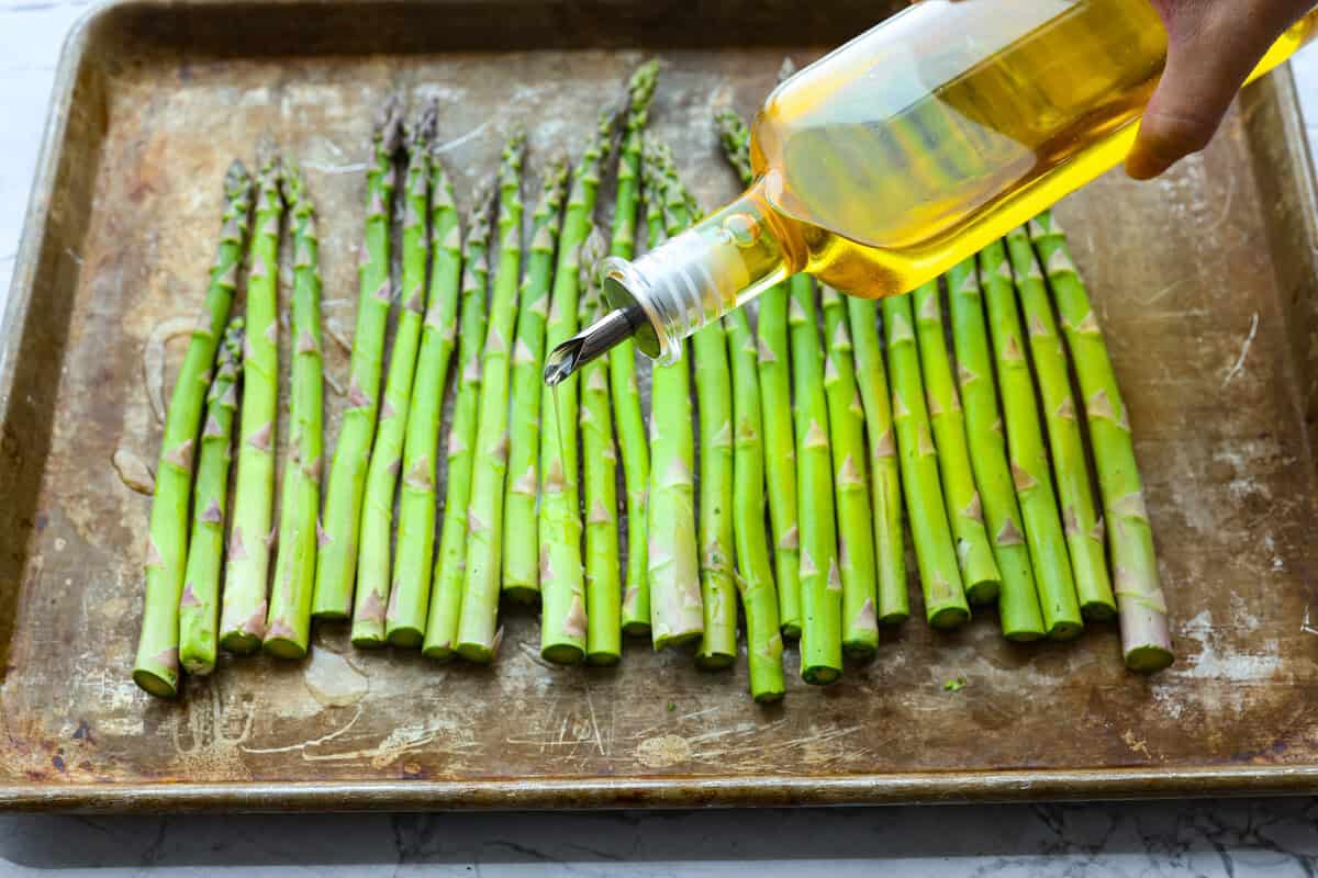 You'll love the combination of flavors in this roasted lemon parmesan garlic asparagus! It's a quick and easy side dish bursting with parmesan, garlic, and a hint of lemon to brighten it all. This is a side that you will make again and again! First photo of drizzling olive oil on the asparagus.