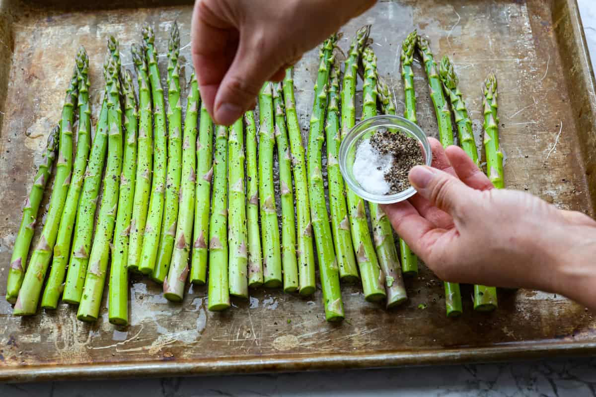 You'll love the combination of flavors in this roasted lemon parmesan garlic asparagus! It's a quick and easy side dish bursting with parmesan, garlic, and a hint of lemon to brighten it all. This is a side that you will make again and again! Second photo of seasoning the asparagus with salt and pepper.