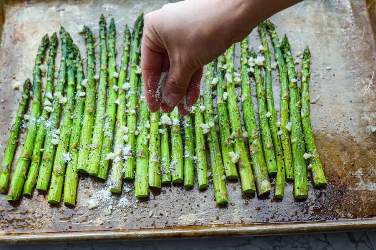 You'll love the combination of flavors in this roasted lemon parmesan garlic asparagus! It's a quick and easy side dish bursting with parmesan, garlic, and a hint of lemon to brighten it all. This is a side that you will make again and again! Third photo of adding parmesan cheese and garlic to the roasted asparagus.