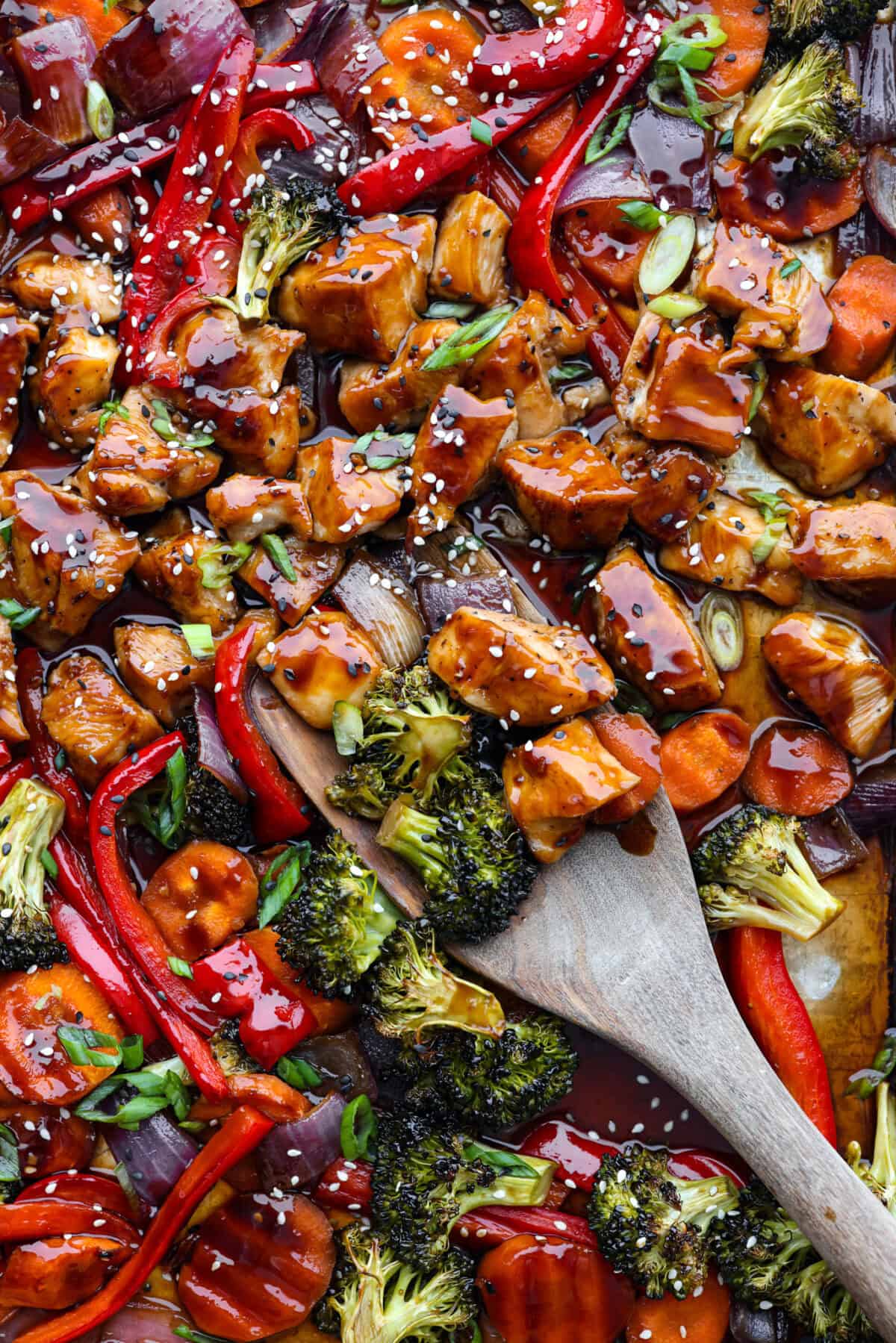 Close view of sheet pan teriyaki chicken with vegetables with a wood spatula.