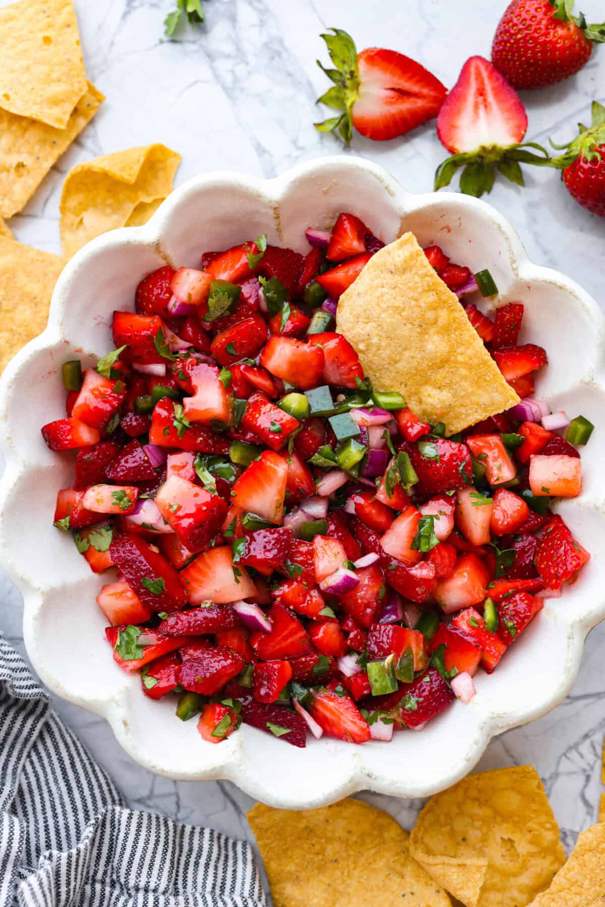 Top view of strawberry salsa in a scalloped bowl with a tortilla chip in it. 