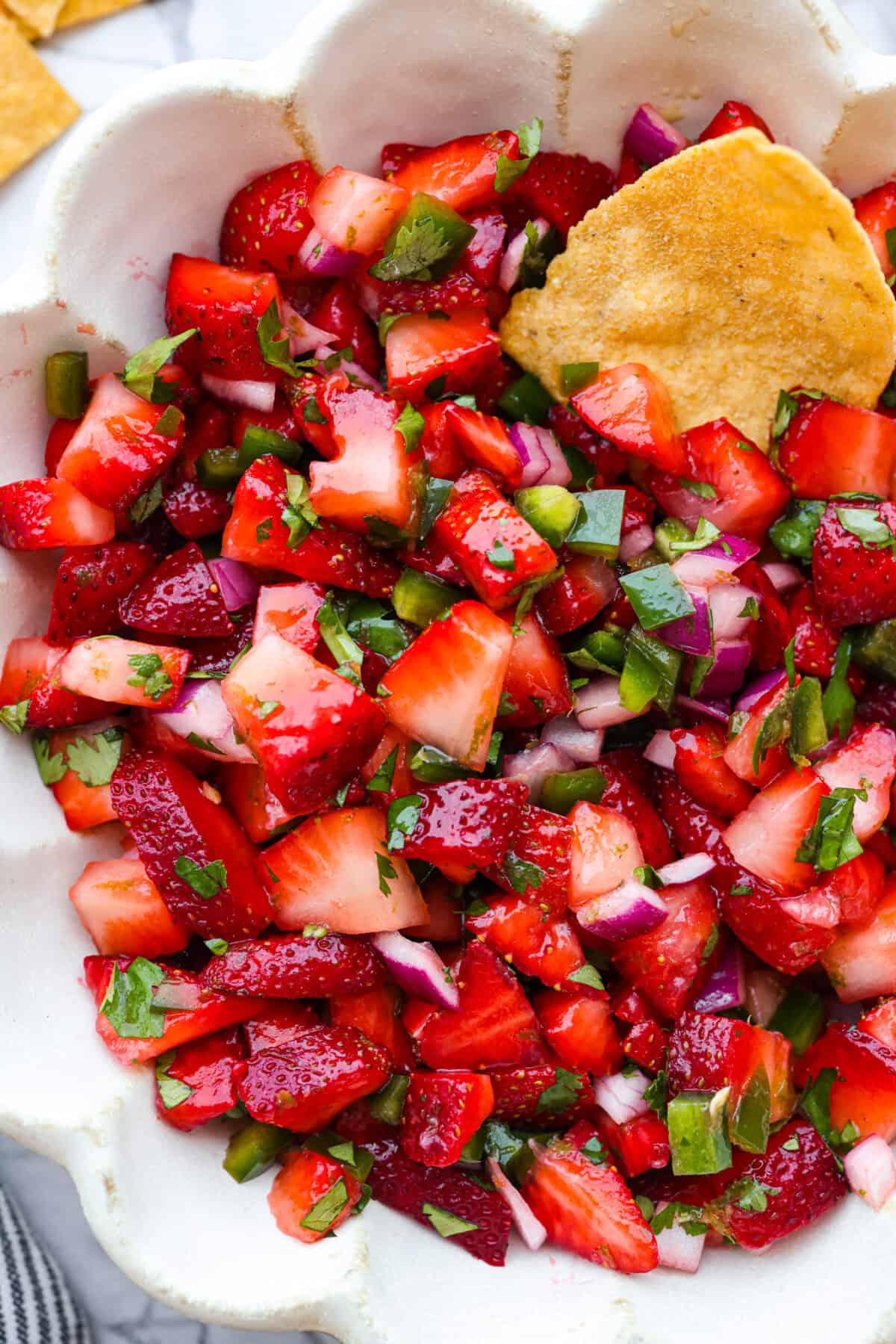 A close up of strawberry salsa in a bowl with a chip. 