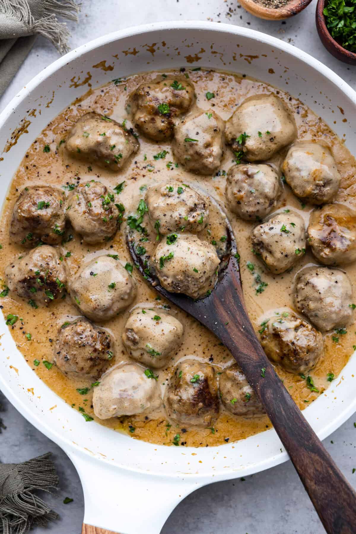 A pan filled with cooked Swedish Meatballs with a wooden spoon. 