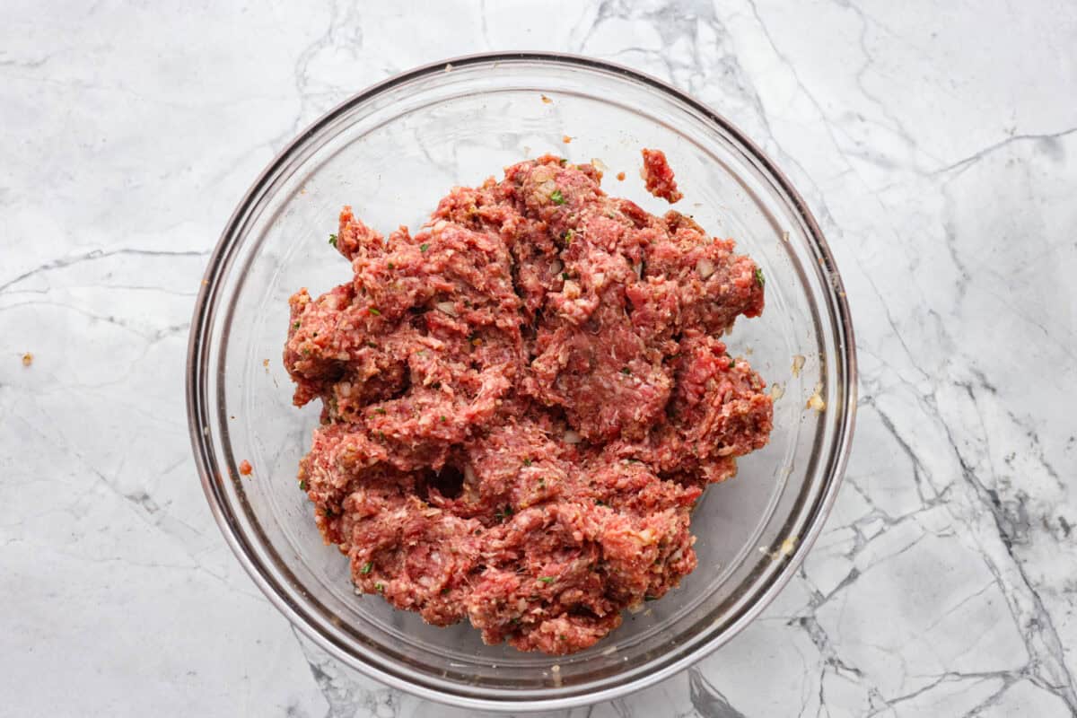 Ground beef and spices combined in a glass bowl.