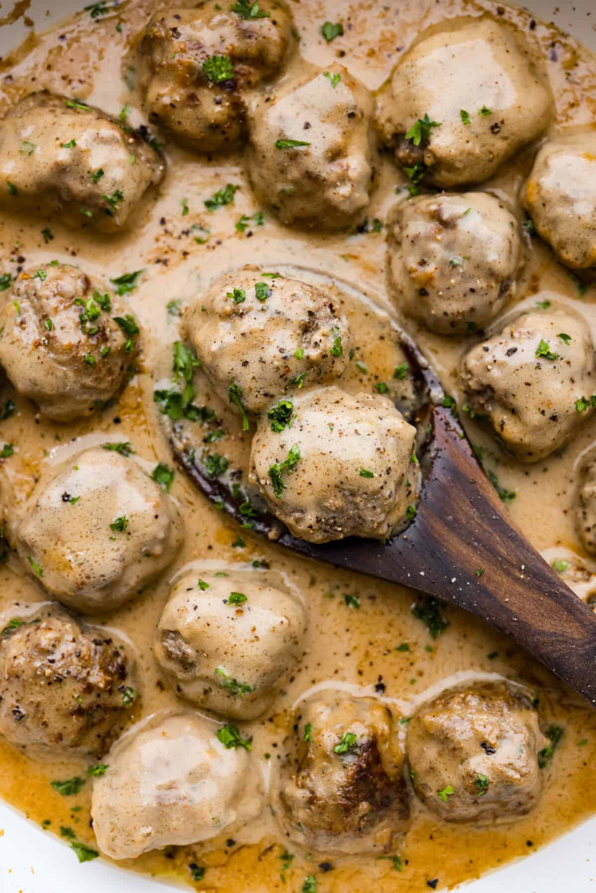 A close up of Swedish meatballs being served on a wooden spoon. 