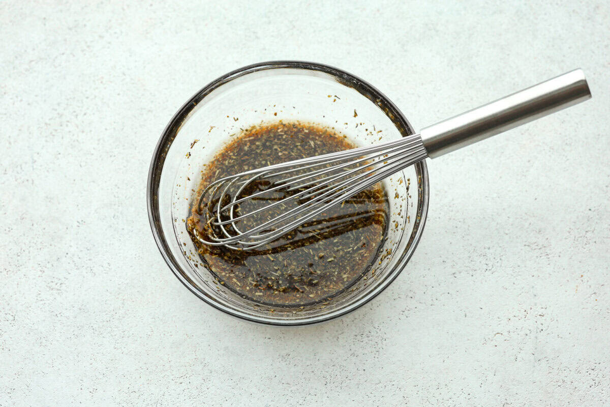 A whisk in a glass bowl with triple tip marinade. 