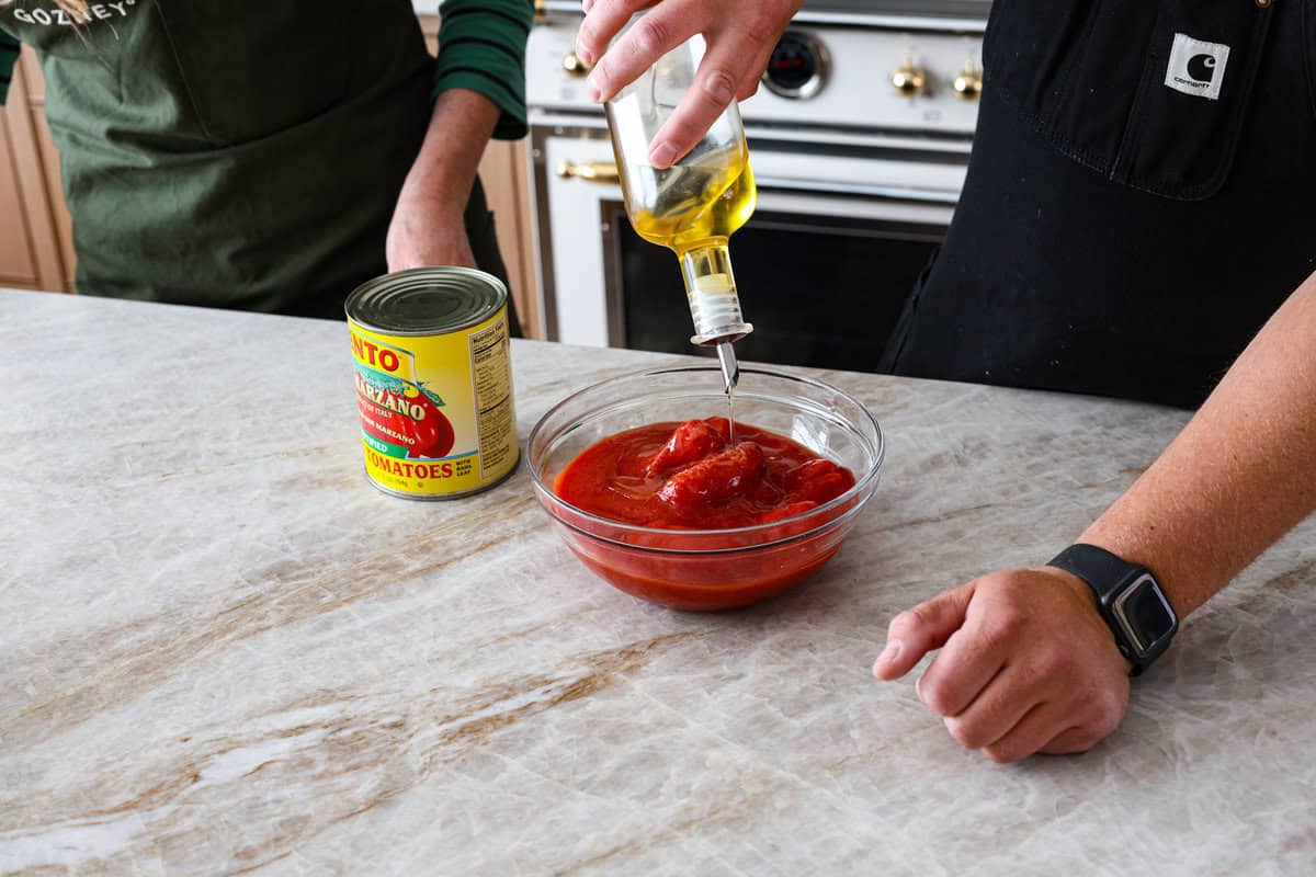 This is the perfect beginner's guide for making wood-fired pizza dough! Pizza expert, Chef Brandon Price, taught me how to make authentic homemade pizza, and now you get to learn too! First photo of the canned tomatoes and olive oil added to a bowl.